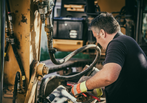 Construction worker repairing a piece of hydraulic heavy machinery.