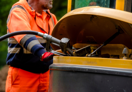 Builder in safety gloves filling excavator with diesel fuel on building site fuel theft from construction site on a rise